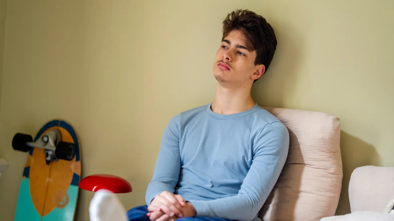 Jongen zit op bed en kijkt voor zich uit