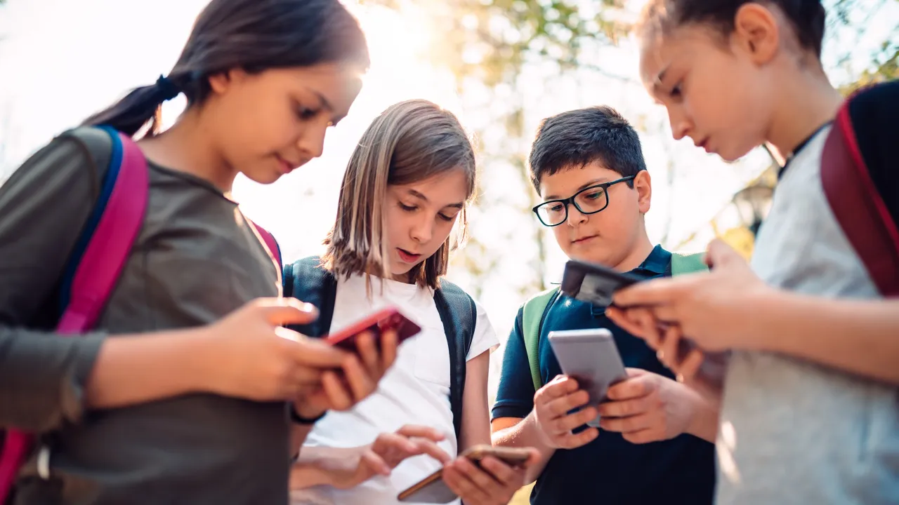 Vier kinderen staan in een kring. Ze houden een telefoon vast