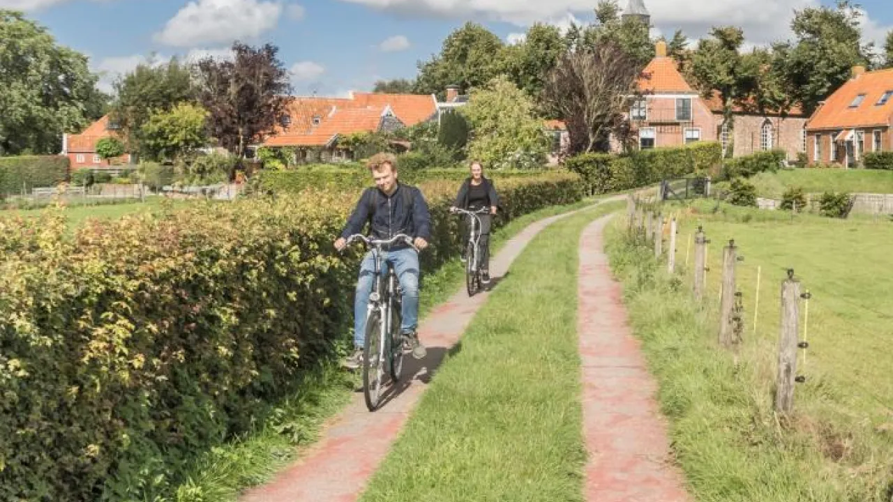 Twee mensen fietsen over pad naast weiland.