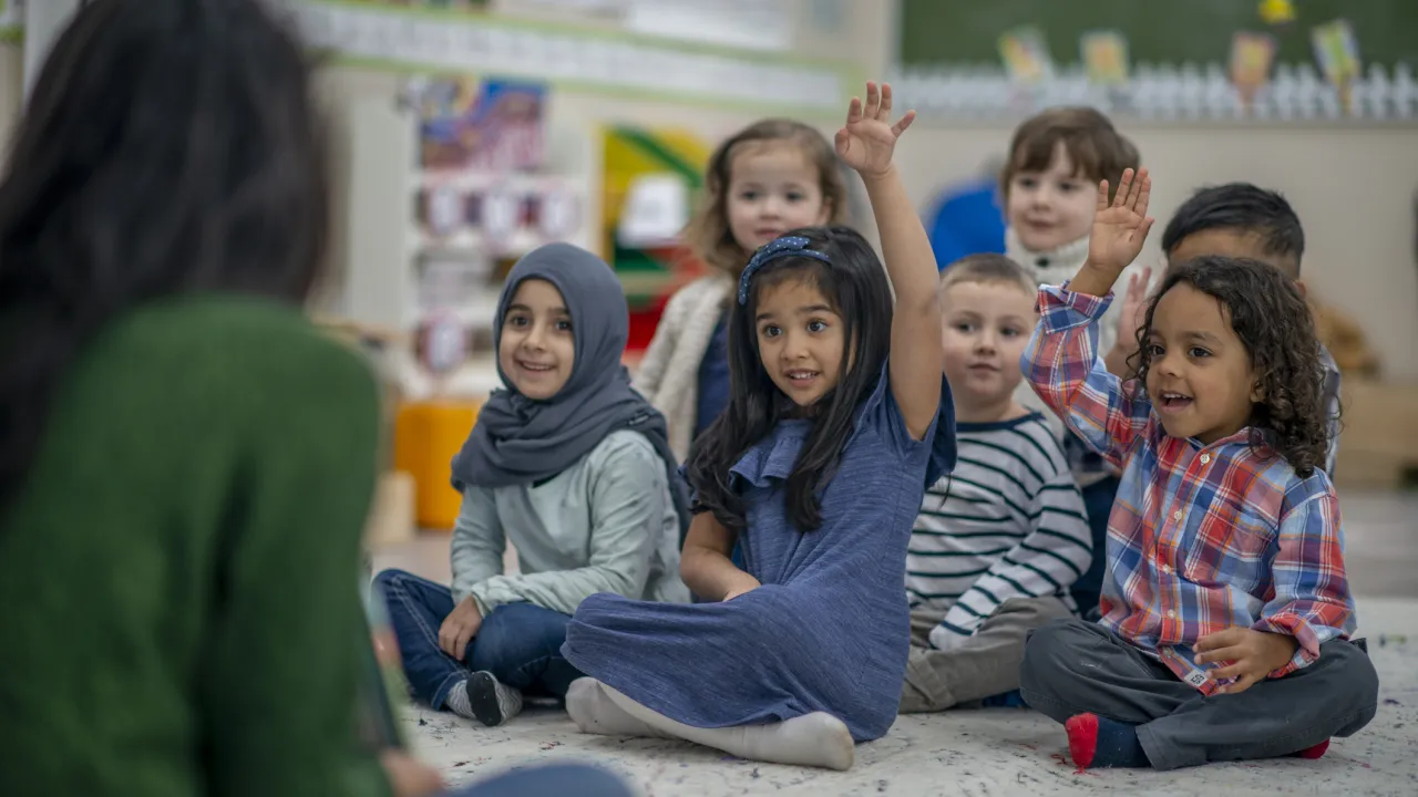 Groep jonge kinderen zit op de grond in de klas. 