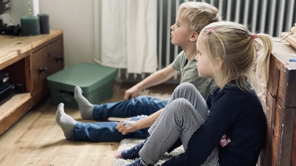 Twee kinderen zitten in de woonkamer op de grond en kijken tv
