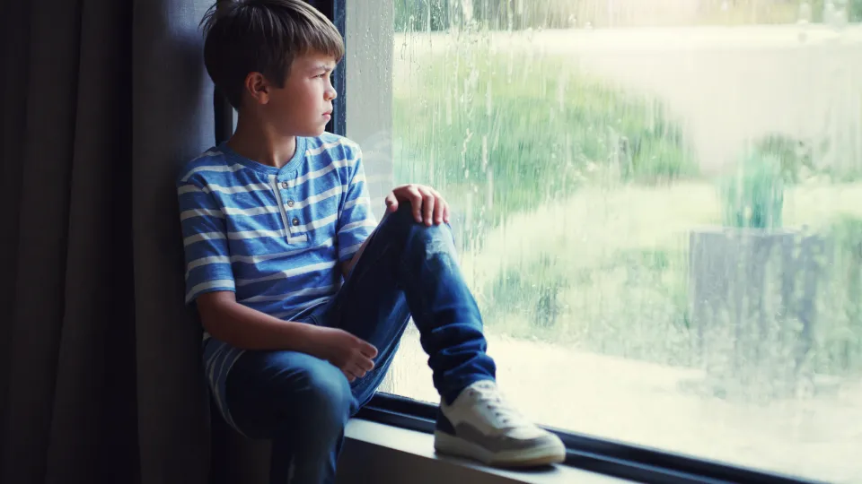 Jongen zit op de vensterbank voor het raam en kijkt naar buiten.