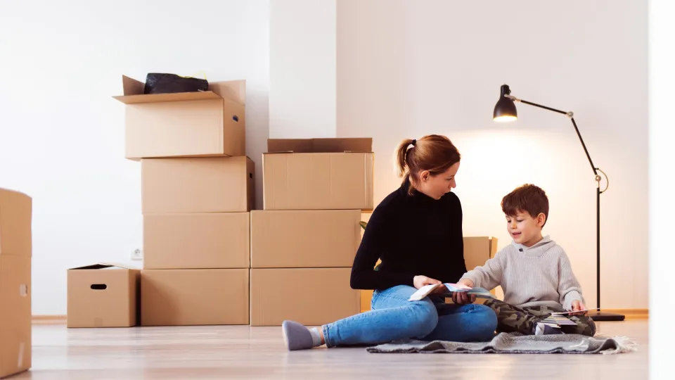 Moeder en zoon zitten op de grond in kamer. Op de grond staan verhuisdozen