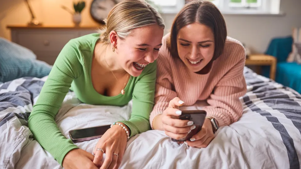 Lachende tienermeisjes kijkend liggend op bed op een telefoon