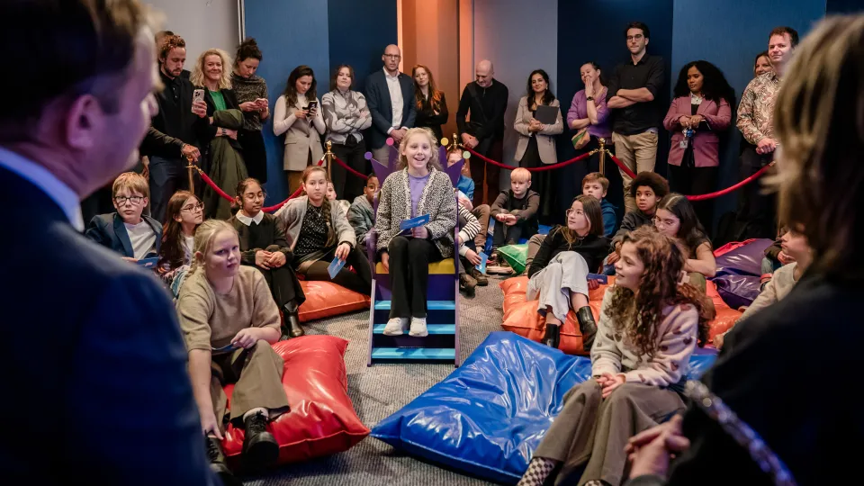 Kinderpersconferentie Kinderrechtentoets. Een zaal vol kinderen stelt vragen aan Kinderombudsvrouw Margrite Kalverboer en Staatssecretaris Struycken