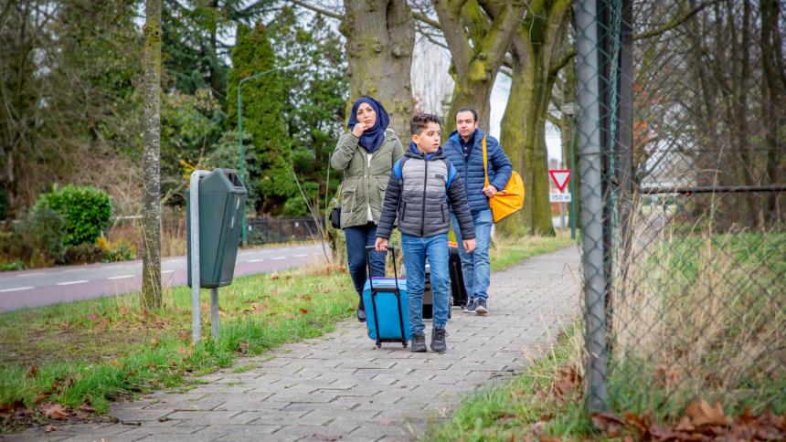 Een jongen en ouders met koffers lopen bij een opvangcentrum