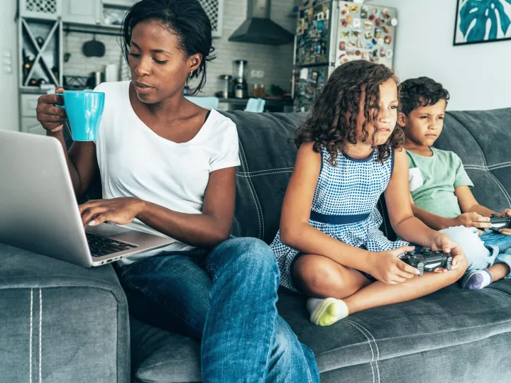 Een moeder zit met haar kinderen op de bank. Moeder kijkt op haar laptop