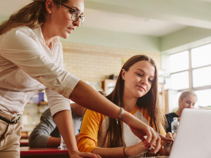 Een tienermeisje werkt in de klas op haar laptop en wordt geholpen door haar docent