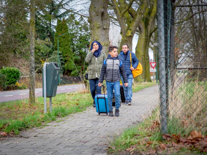 Een jongen en ouders met koffers lopen bij een opvangcentrum