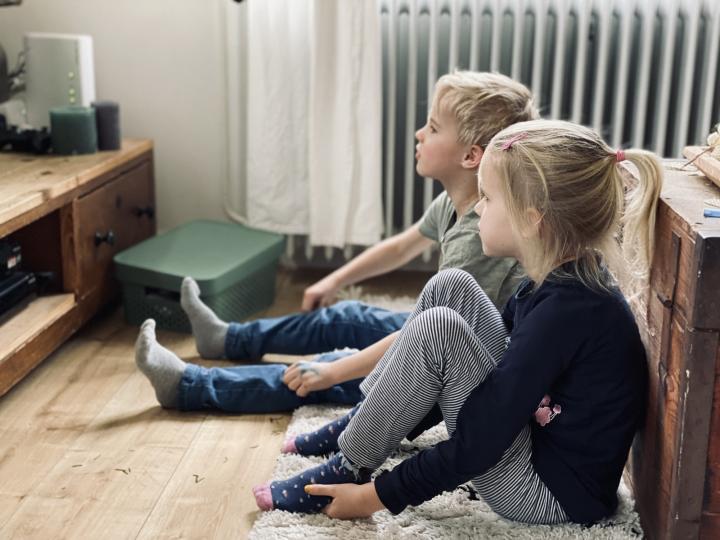 Twee kinderen zitten in de woonkamer op de grond en kijken tv