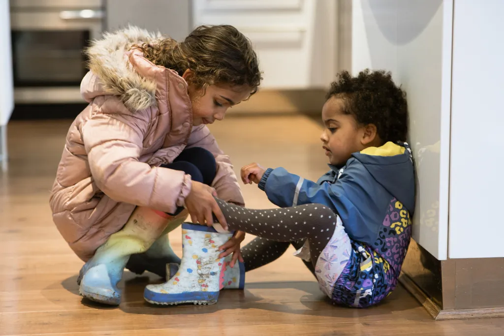 twee kindjes helpen elkaar met laarsjes aantrekken